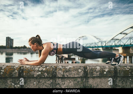 Young Sport Frau tun plank Übung auf der Wand während outdoor Cross Training durch den Fluss fokussiert. Stockfoto