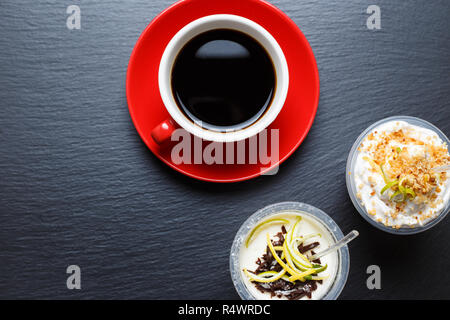 Rot Tasse Kaffee mit Take away Desserts auf schwarzem Schiefer Hintergrund Stockfoto