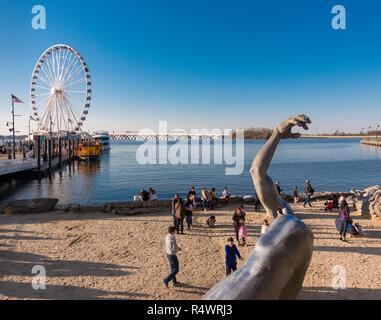 NATIONAL Harbor, Maryland, USA - Das Erwachen Skulptur und die Leute am Strand, mit Hauptstadt Rad Fahrgeschäft auf der linken Seite. Stockfoto