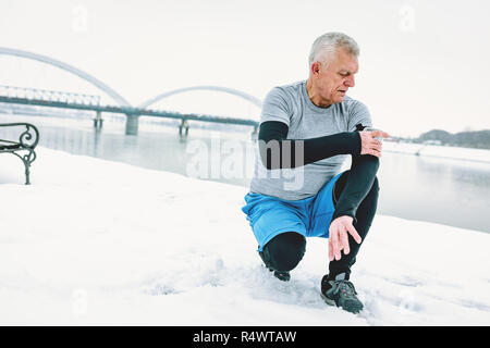 Aktive ältere Menschen überprüfen Mobiltelefon während der Übungen durch den Fluss im Winter Training im Freien. Kopieren Sie Platz. Stockfoto