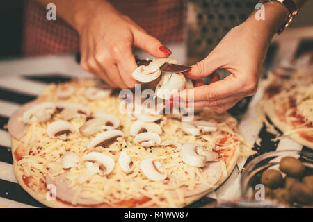 Close-up ist eine junge Frauen Hände schneiden Pilze und setzen auf die Pizza Teig. Stockfoto