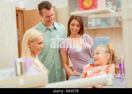 Glückliche Familie zu Besuch in der Zahnarztpraxis. Weiblichen Zahnarzt im Gespräch mit kleines Mädchen, ihren Eltern steht neben ihr. Stockfoto