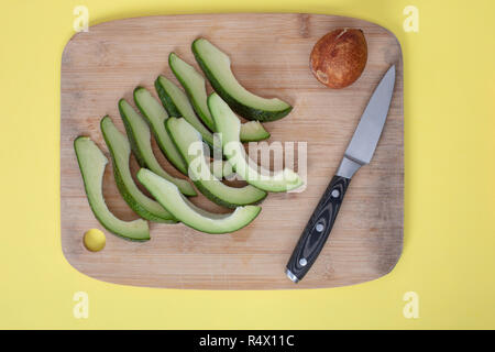 Avocado Schichten und Core auf Schneidebrett mit Messer auf gelben Hintergrund. Ansicht von oben. Flach Muster, Design Element für das Etikett. Stockfoto