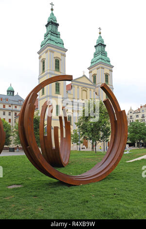 BUDAPEST, Ungarn - 13. Juli: Kunst Installation und Innerstädtische Pfarrkirche in Budapest am 13. Juli 2015. Zeitgenössische Kunst Skulptur vor der Gotischen Stockfoto