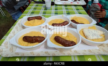 Typische italienische Polenta (gekochtes Maismehl) Mahlzeiten in Einweggeschirr, mit gebratenen Würstchen oder Gorgonzola Blau Käse während ein beliebtes Mittagessen Stockfoto