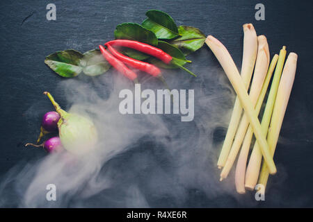 Zutaten für populäre thailändische Suppe Tom - Yum Kung. Kalk, Galgant, roter Chili, Cherry Tomaten, Zitronengras und Kaffernlimette Blatt auf dem Schwarzen Brett. Flach. Blick von oben. Stockfoto