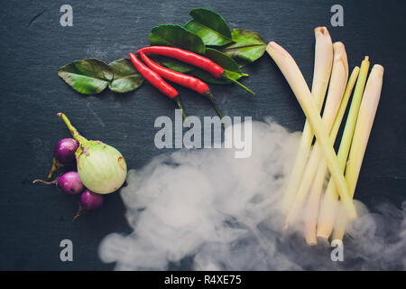 Zutaten für populäre thailändische Suppe Tom - Yum Kung. Kalk, Galgant, roter Chili, Cherry Tomaten, Zitronengras und Kaffernlimette Blatt auf dem Schwarzen Brett. Flach. Blick von oben. Stockfoto