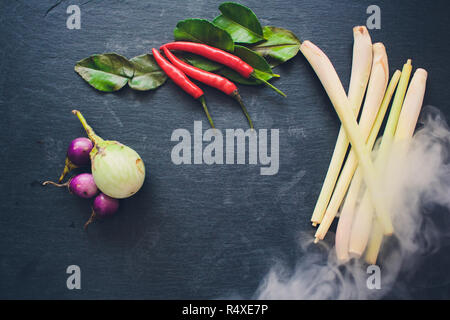 Zutaten für populäre thailändische Suppe Tom - Yum Kung. Kalk, Galgant, roter Chili, Cherry Tomaten, Zitronengras und Kaffernlimette Blatt auf dem Schwarzen Brett. Flach. Blick von oben. Stockfoto