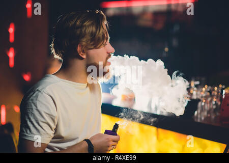 Junge schöne hipster Mann mit Bart im Cafe Sitzen mit einer Tasse Kaffee, vaping und löst eine Wolke aus Dampf. Stockfoto