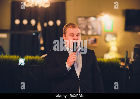 Junger Mann mit Mikrofon auf grauem Hintergrund, die mit Mikrofon in Studio Konzept. Menschliche Gefühle und Mimik Konzepte. Stockfoto