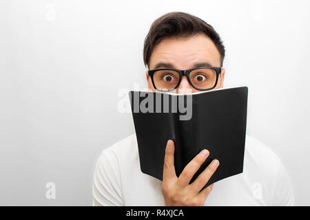 Bild der männlichen brunette auf Kamera. Er hat schwarzes Buch in den Händen. Er war eine Brille. Junge Mann ist aufgeregt. Auf weißem Hintergrund isoliert. Stockfoto