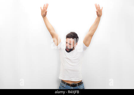 Sehr glückliche junge Mann steht und schaut nach unten. Er hält die Hände nach oben. Guy ist erstaunt. Auf weissem Hintergrund. Stockfoto