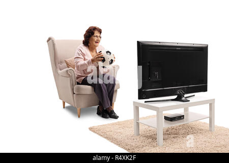 Ältere Frau im Sessel mit Fußball zu sitzen und ein Spiel im TV auf weißem Hintergrund Stockfoto