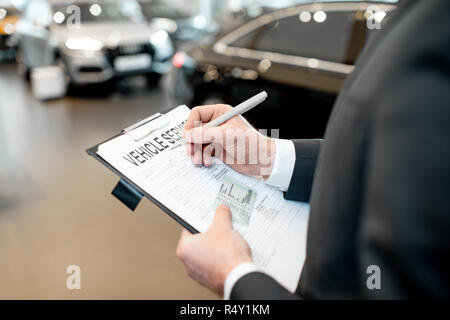 Manager ausfüllen Fahrzeug Service Dokumente Ordner mit Führerschein in den Showroom mit dem Auto auf dem Hintergrund Stockfoto