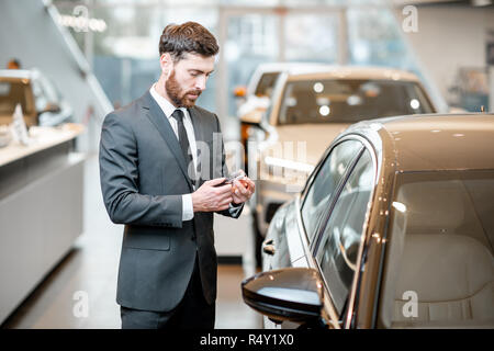 Happy Geschäftsmann holding Tasten vor seinem neuen Auto stehend im Showroom Stockfoto