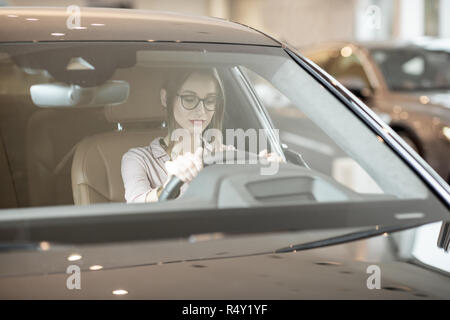 Junge Frau bei der Auswahl eines neuen Auto sitzen auf dem Fahrersitz eines Luxuswagens im Showroom Stockfoto