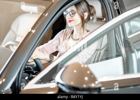 Junge Frau bei der Auswahl eines neuen Auto sitzen auf dem Fahrersitz eines Luxuswagens im Showroom Stockfoto