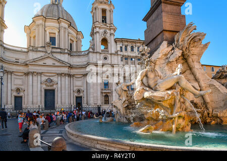 Touristen im Schatten der Sant'Agnese in Agone Kirche entspannen, da das Sonnenlicht trifft die Bernini gestaltete Brunnen der vier Flüsse auf der Piazza Navona. Stockfoto