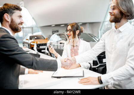 Young Business Paar Hände schütteln in einen Deal mit Verkäufer am Stand den Kauf oder die Vermietung von Auto im Showroom Stockfoto