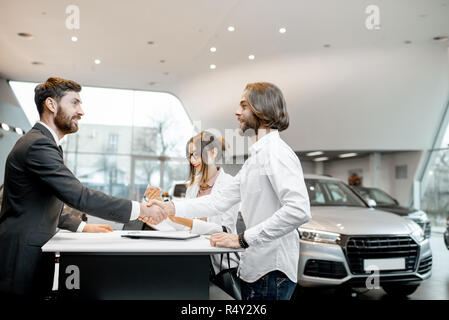 Young Business Paar Hände schütteln in einen Deal mit Verkäufer am Stand den Kauf oder die Vermietung von Auto im Showroom Stockfoto