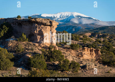 Red Rock Formation mit den schneebedeckten Gipfeln der Sangre de Cristo Bergkette in der Ferne in der Nähe von Santa Fe, New Mexico Stockfoto