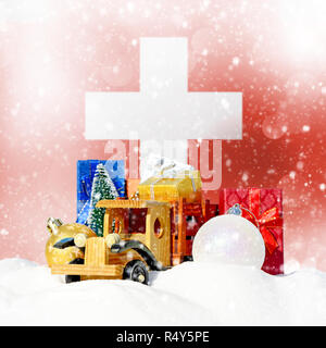 Weihnachten Hintergrund. Spielzeug-LKW mit Geschenken, Neues Jahr Tanne, Kugeln im Schneetreiben und Schweizer Flagge Stockfoto