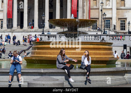 Touristen sitzen am Rande der Brunnen am Trafalgar Square mit der Nationalgalerie im Hintergrund London England UK Stockfoto