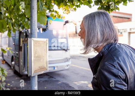 Attraktive Frau wartet auf den Bus beim Prüfen der Zeitpläne Stockfoto