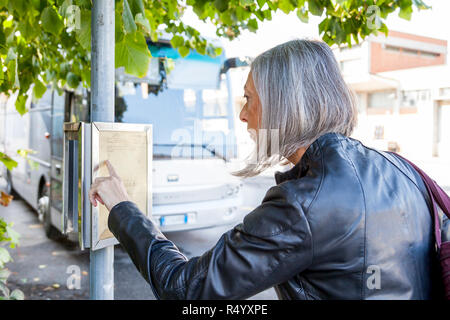 Attraktive Frau wartet auf den Bus beim Prüfen der Zeitpläne Stockfoto