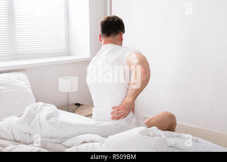 Mann sitzt auf dem Bett, Rückenschmerzen Stockfoto