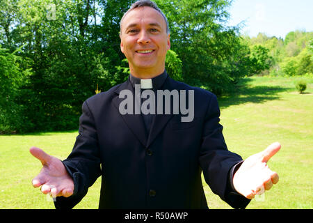 Ein katholischer Priester uns ist einladend in der Freude. Er schaut uns mit Optimismus, seine Arme öffnen in Frieden. Stockfoto