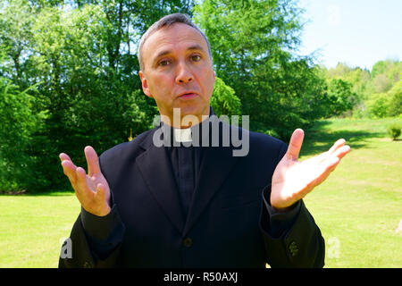 Ein katholischer Priester uns ist einladend in der Freude. Er schaut mit Vertrauen an uns, seine Arme öffnen in Frieden. Stockfoto