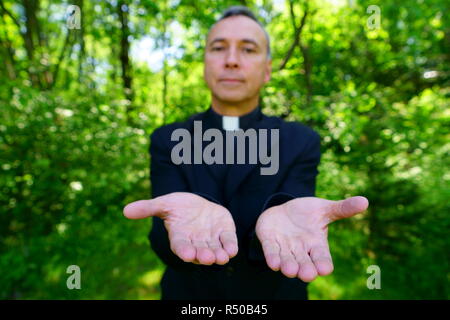 Ein katholischer Priester uns ist einladend in der Freude. Er schaut mit Vertrauen an uns, seine Arme öffnen in Frieden. Konzentrieren Sie sich auf die Hände. Stockfoto