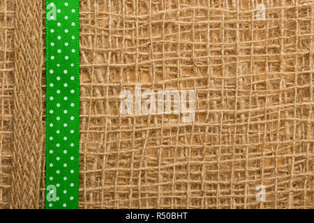 Polka Dot Green Ribbon auf Braun mesh Material, natürliche Sackleinen Hintergrund Stockfoto