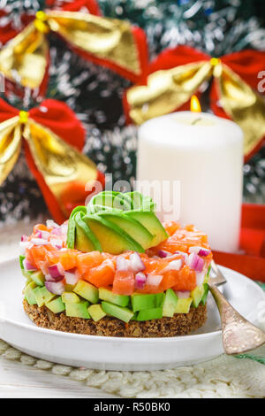 Lachstatar (Forellen) mit Avocado und rote Zwiebel auf Roggenbrot. Einstimmung auf Weihnachten und das Neue Jahr. Einen leichten Snack für Gourmets. Selektiver Fokus Stockfoto