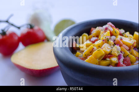 Mango Salsa in einem Stein Schüssel mit Zutaten in den Hintergrund Stockfoto