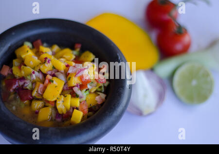 Mango Salsa in einem Stein Schüssel mit Zutaten in den Hintergrund Stockfoto