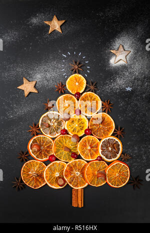 Weihnachtsbaum aus getrockneten Orangen, Zimt, Preiselbeeren, Muttern und Sternanis auf dunklem Hintergrund. Von oben, vertikale Komposition gesehen Stockfoto