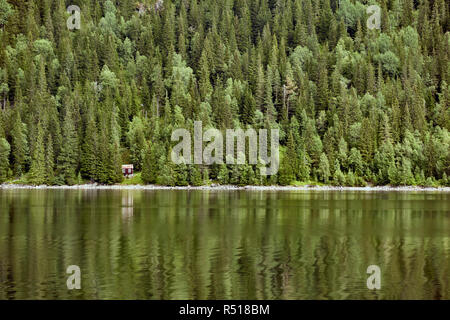 Kleine Hütte an einem See in Norwegen umgeben mit grünen Pinienwald im See spiegeln. Stockfoto