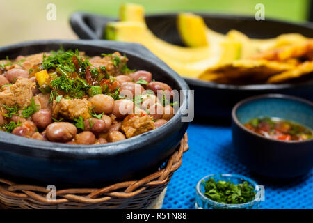 Bohnen mit Schweinefleisch serviert mit Avocado und patacon auf traditionelle schwarze Keramik Geschirr Stockfoto