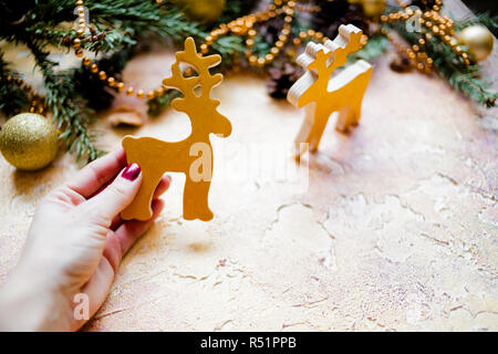 Weihnachten Komposition mit Tannenzweigen und pinienzapfen auf Holz- Hintergrund. Weihnachtskarte mit Weihnachten rustikale Dekorationen. Goldene Holz- Rotwild in weiblicher Hand. Holzspielzeug. Frohes neues Jahr Konzept. Platz kopieren Stockfoto