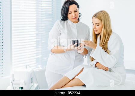 Frau mit kosmetikerin erhält Termin für nächsten Besuch, verwendet Smartphone im Salon Stockfoto
