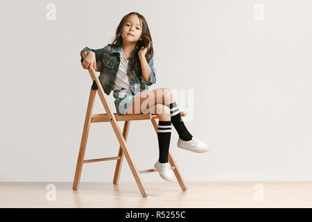 Volle Länge Portrait von niedlichen kleinen Kind Mädchen in der stylischen Jeans Kleidung bei Kamera suchen und lächelnd gegen Weiße studio Wand. Kids Fashion Concept Stockfoto