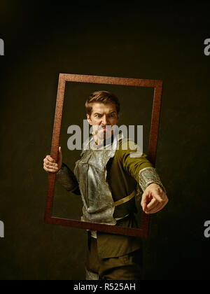 Mittelalterliche wütend Ritter auf dunklen Studio Hintergrund. Portrait in Low Key der brutalen Mann in tradishional Retro Kostüm der spanischen Hidalgo. Menschliche Emotionen, Vergleich von Epochen und Mimik Konzept Stockfoto