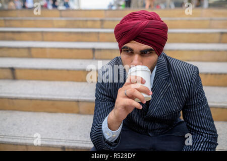 Indischer Geschäftsmann sitzen draußen in der Stadt und trinken Kaffee Stockfoto