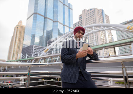 Indischer Geschäftsmann mit Turban im Freien in der Stadt mit Handy Stockfoto