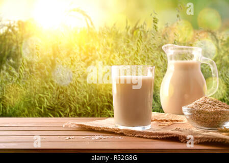 Oat Drink in Glas und Getreideflocken auf Holz Tisch in der Natur. Horizontale Komposition. Ansicht von vorn Stockfoto
