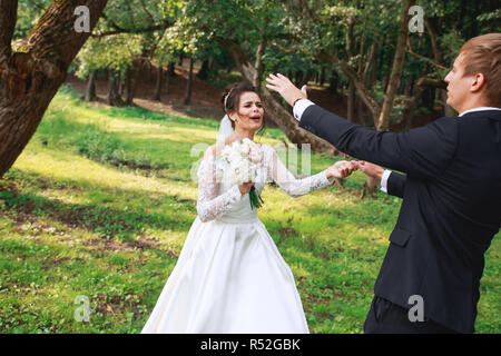 Gerne hübscher Bräutigam und schöne Braut im weißen Kleid lachen und tanzen im Park Stockfoto