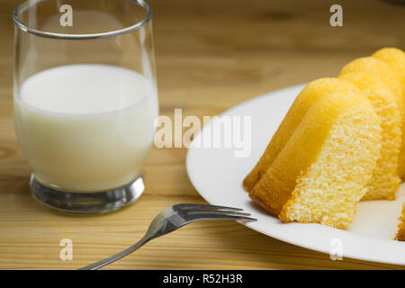 Nahaufnahme der hausgemachten Zitronenkuchen auf einem weißen Teller und ein Glas frische Milch auf einen hölzernen Tisch. Stockfoto