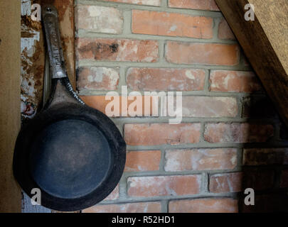 Vintage Gusseisen Skillet Übergabe auf alten Ziegelmauer mit Holzbalken in der Ecke. Interieur eines Hauses, Kastanie Square Historic Village, McKinney, Texas Stockfoto